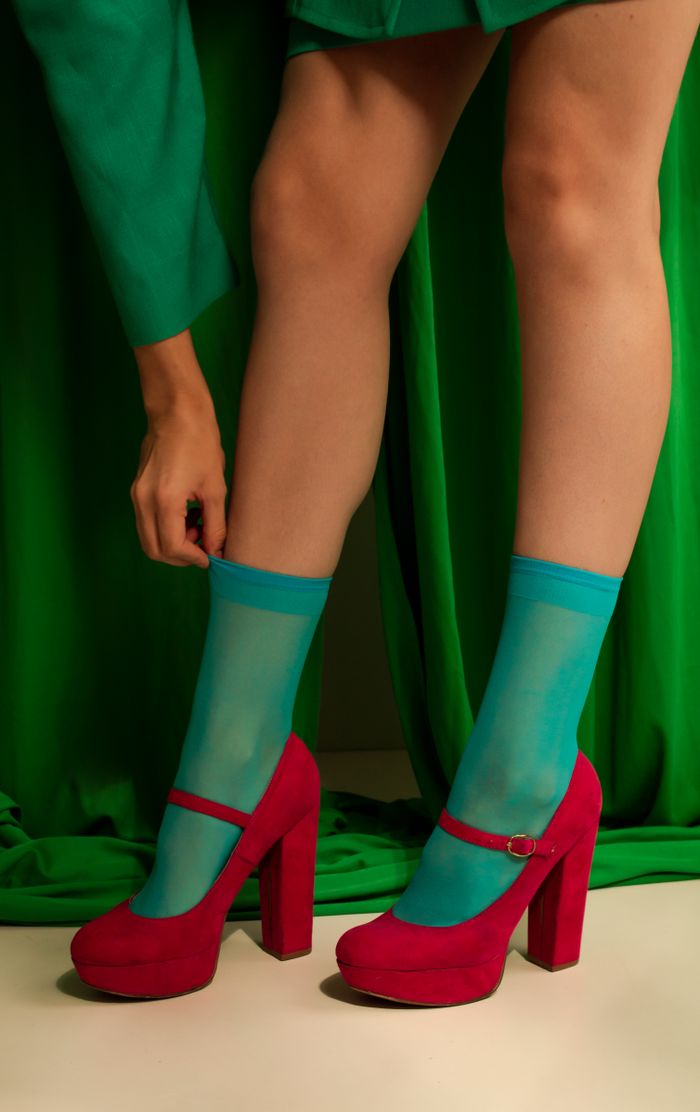 A stylish look with bright turquoise socks and bold pink heels against a green background.